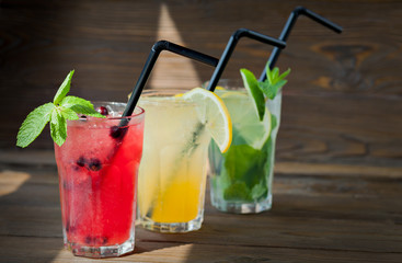 Three different refreshing lemonade with lemon and lime on a wooden background. Summer drink.