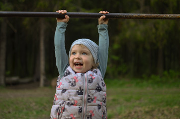 Fototapeta premium blue-eyed girl child hanging on the bar for pull-ups