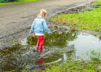 Little girl with red boots walking through the puddle