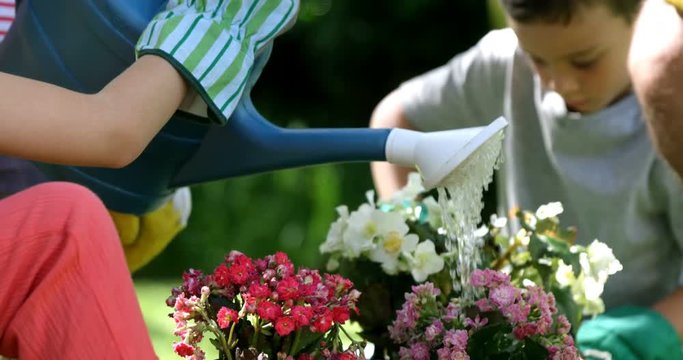 Close up on a cute girl is watering flowers in front of her family in the garden