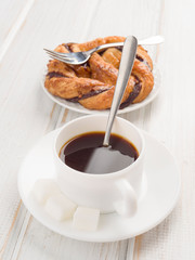 cup of black coffee with pastry loop on wood