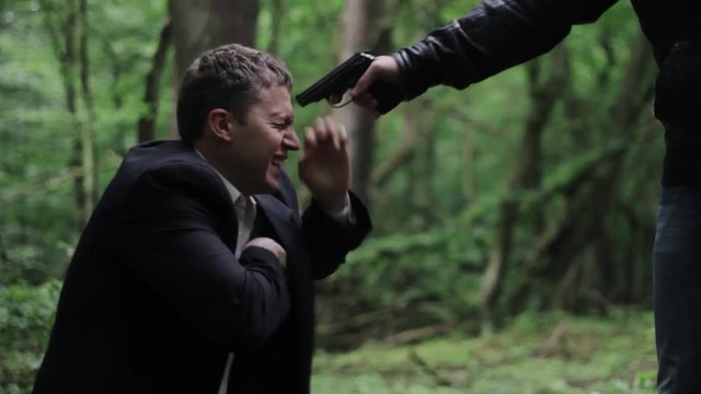 	Businessman kneels in the woods and begs for mercy thug.