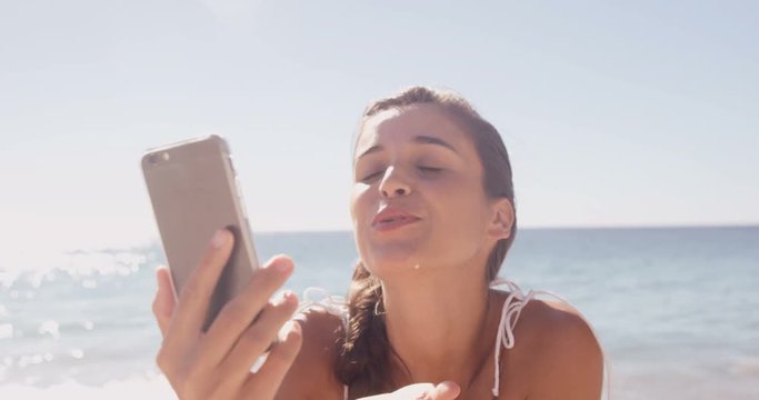 Woman blowing a kiss in front of her smartphone at the beach 