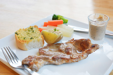 pork steak with vegetable on a plate and wooden table background