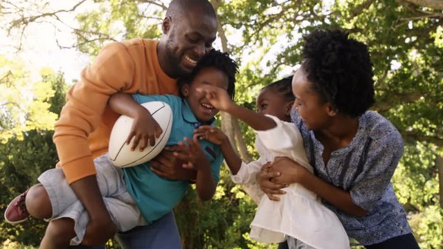 Cute family is playing rugby in a park 