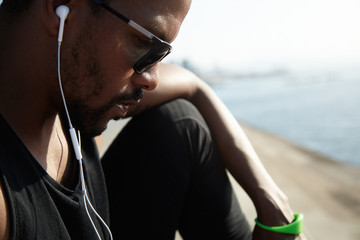 Young African American rapper in black top listening to new tracks outside under blue sky. Handsome...