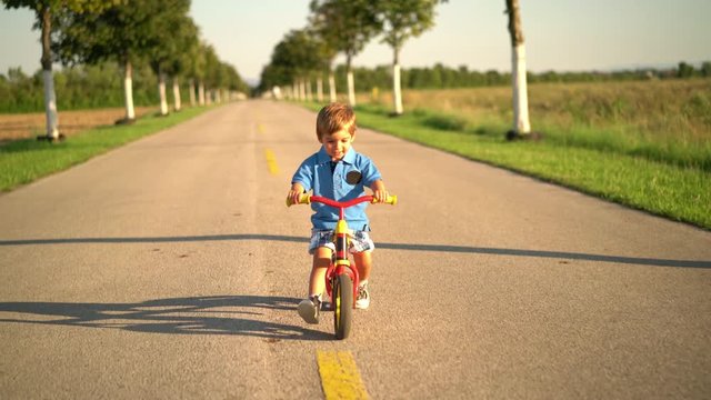 4k footage, little boy learning to ride bicyle with walking bike on empty street in rural landscape
