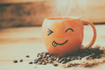smile face hot coffee cup with bean on wood background, happy coffee time concept.