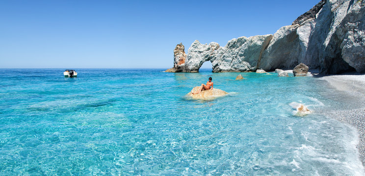 Strand mit Felsen, Boot und Frau beim Sonnenbad 