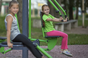 Fototapeta na wymiar Little girls sitting on exercise equipment in the public park.