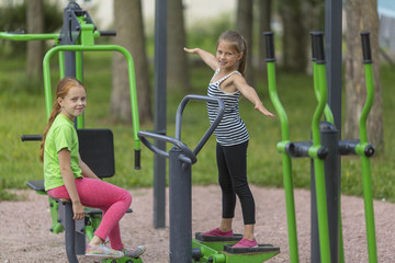 Fototapeta na wymiar Two little cute girls warming up on the Playground in the Park. Healthy lifestyle..