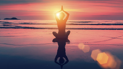 Silhouette yoga woman in Lotus pose on beach during sunset. With the reflection in the water. Harmony and meditation.
