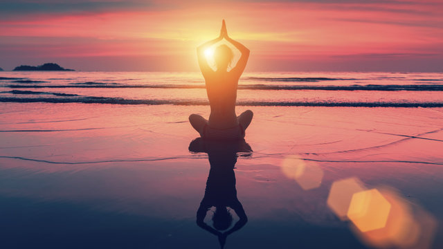 Silhouette yoga woman in Lotus pose on beach during sunset. With the reflection in the water. Harmony and meditation.