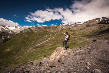 Young woman hiker with backpack standing on top of a mountain and enjoying valley view