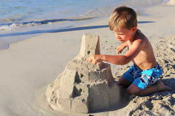 A young blond boy building sand castle in a beach in Corsica