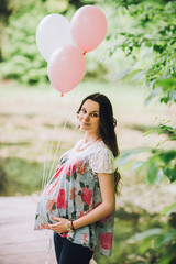 Young beautiful pregnant woman relaxing at the lake. Pregnacy with baloons on pier