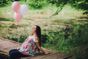 Young beautiful pregnant woman relaxing at the lake. Pregnacy with baloons on pier