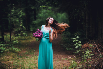 Portrait of a beautiful brunet  pregnant girl in a green dress, dreamy and standing in the forest between the pines. Pregnant woman in the park.