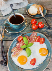 Fototapeta na wymiar Fried eggs, bacon, tomato, toast and a cup of coffee