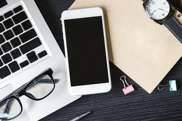 Business workplace from top smart watch, smart phone, glasses, laptop on black wooden desk , retro style vintage tone