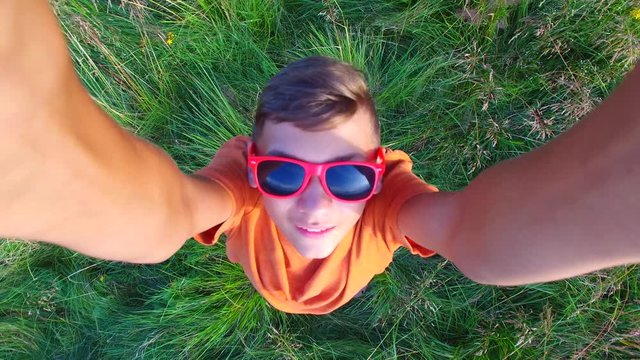 Aerial view of a boy in a red sunglasses having fun in a mountain meadow. Smiling boy is playing with drone.