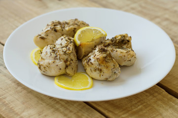 Chicken breasts, chopped and flavored with herbs and lemon sliceces on a white plate, wooden background