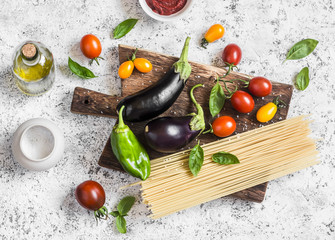 Cooking background. Raw ingredients for making pasta - spaghetti, eggplant, tomatoes, pepper, olive oil, tomato sauce and basil on a rustic cutting board. Top view