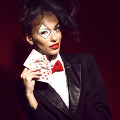 Portrait of a young beautiful lady croupier with an artistic make up holding playing cards with royal flush combination. Gamble and casino concept. Joker image. Studio shot. Close up.