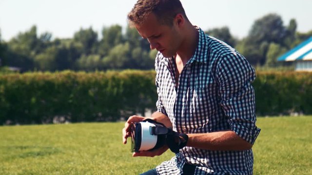 Man in checkered shirt fiddles with appliance while kneeling in large lawn