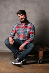 Bearded man in colorful shirt and jeans sitting on a deck