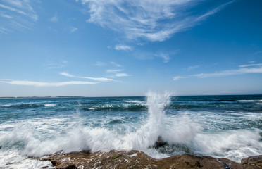 Waves crashing the rocks at Cronulla Beach on a clear blue sky day.