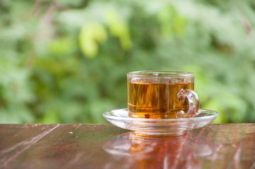 Hot tea cup on wooden table with green nature background, tea time concept