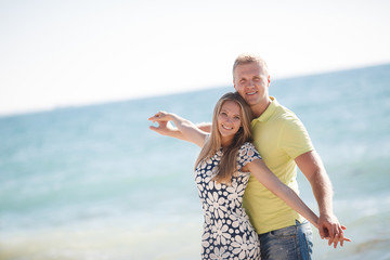 Young happy couple in love,blond man and woman spend time together on the beach on the shore of the blue ocean,standing on the warm sand holding hands on a background of calm sea
