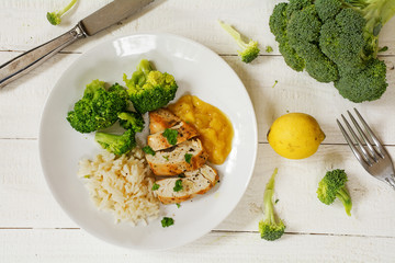 fried chicken breast with a fruity sauce, broccoli and rice on white wood, from above
