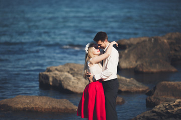 Romantic loving couple posing on stones near sea, blue sky