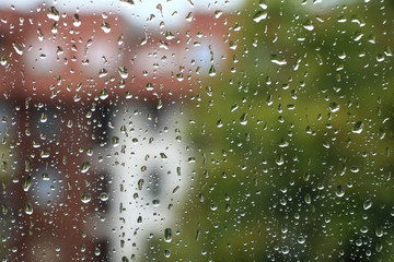 Rain drops on window with building and green tree in background 