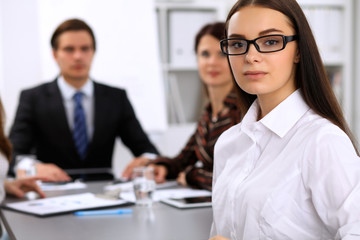 Portrait of a young business woman against a group of business people at a meeting.