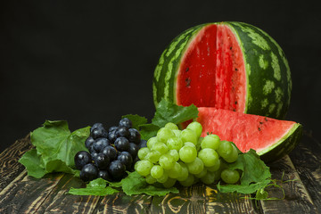 Sliced watermelon, red and green grapes on a wooden table