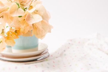 Orange paper flower in small glass with fabric background.