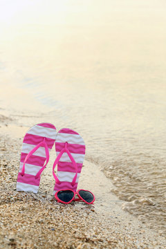 Pink sunglasses with pair of flip flops on the beach sand