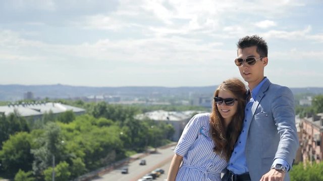 Young couple man and woman stand next to each other, above town, in sunglasses and discuss a beautiful panorama.
