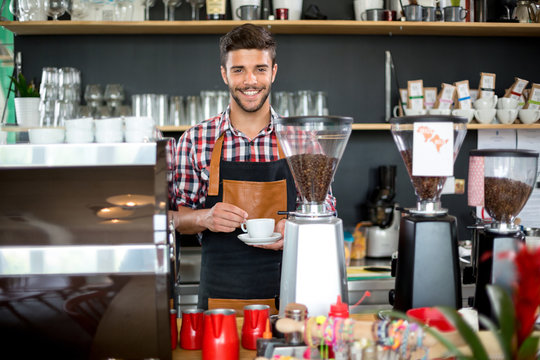 Smiling male waiter holding cup of coffee
