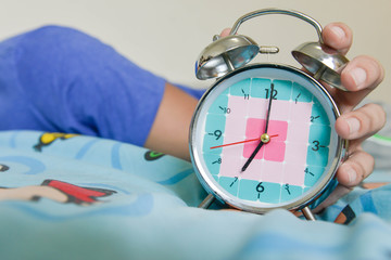 sleepy man is expanding hand to stop the alarm clock that showing time for 7 AM