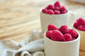 Fresh raspberry in cups on wooden table