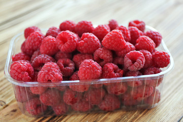 Fresh raspberry in plastic container on table