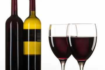 Zwei gefüllte Rotweingläser und Weinflaschen vor weißem Hintergrund. Makro