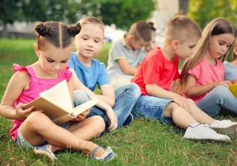 Naklejka na ściany i meble Group of happy kids reading books in park