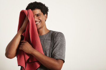 Young attractive black sportsman laughs and wipes his face with a red towel, right half of the face...