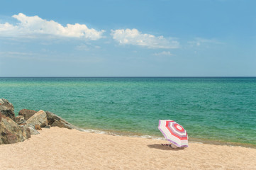 single beach umbrella on empty beach with rocks