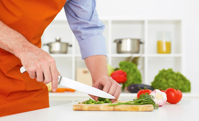 Closeup man's hand with a knife cutting  green onion on a wodden board. Healthy eating, vegetarian food, cooking, dieting and people concept.